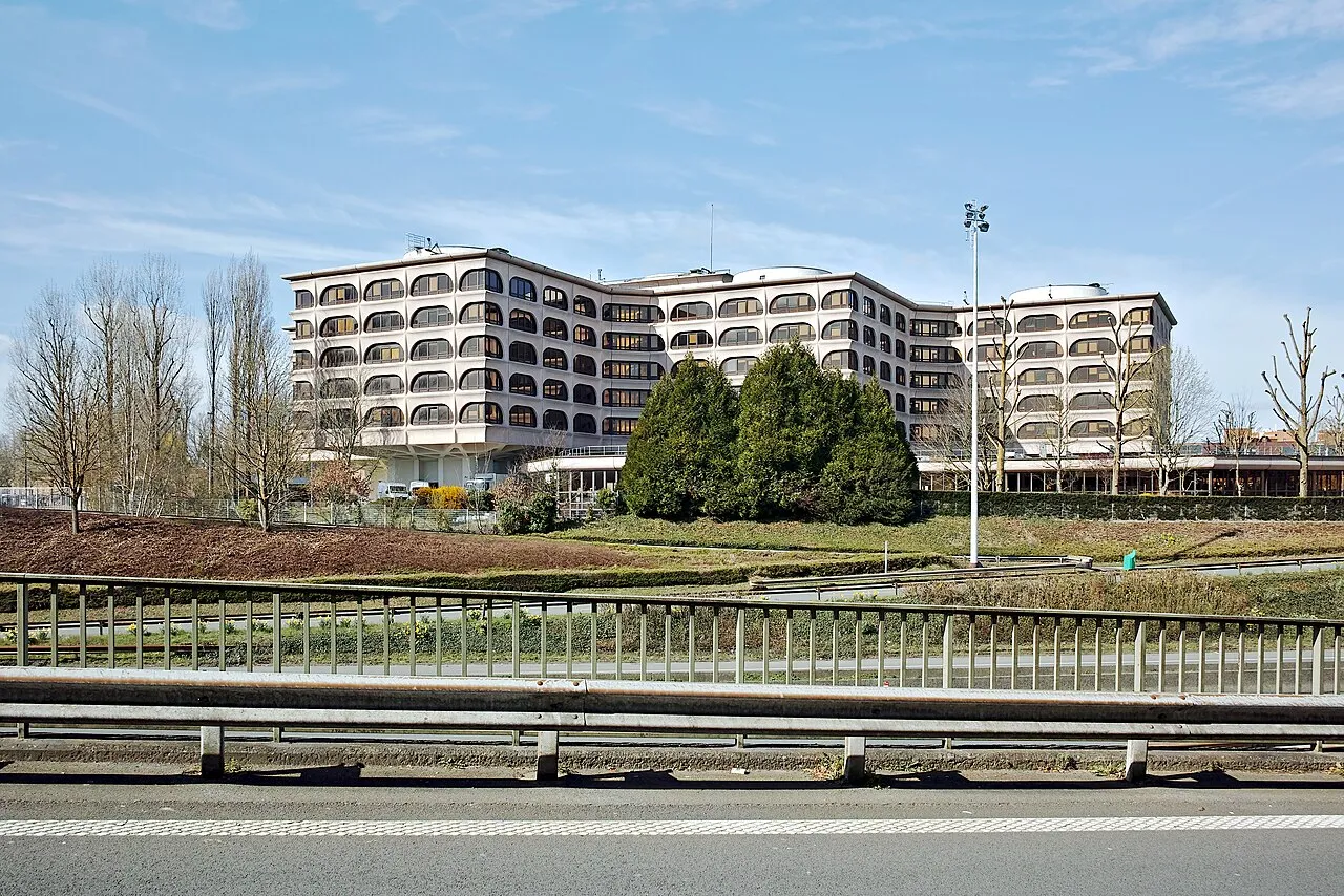 Les bureaux de la Carsat à Villeneuve-d'Ascq, un grand bâtiment blanc aux fenêtres arrondies vu depuis la route