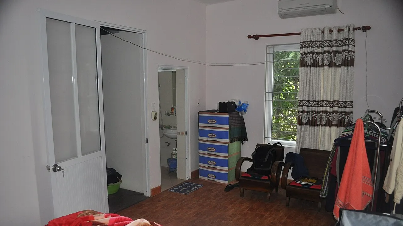 Chambre d'une maison du district de Tây Hồ à Hanoï, avec un climatiseur mural au-dessus de la fenêtre et une salle d'eau attenante