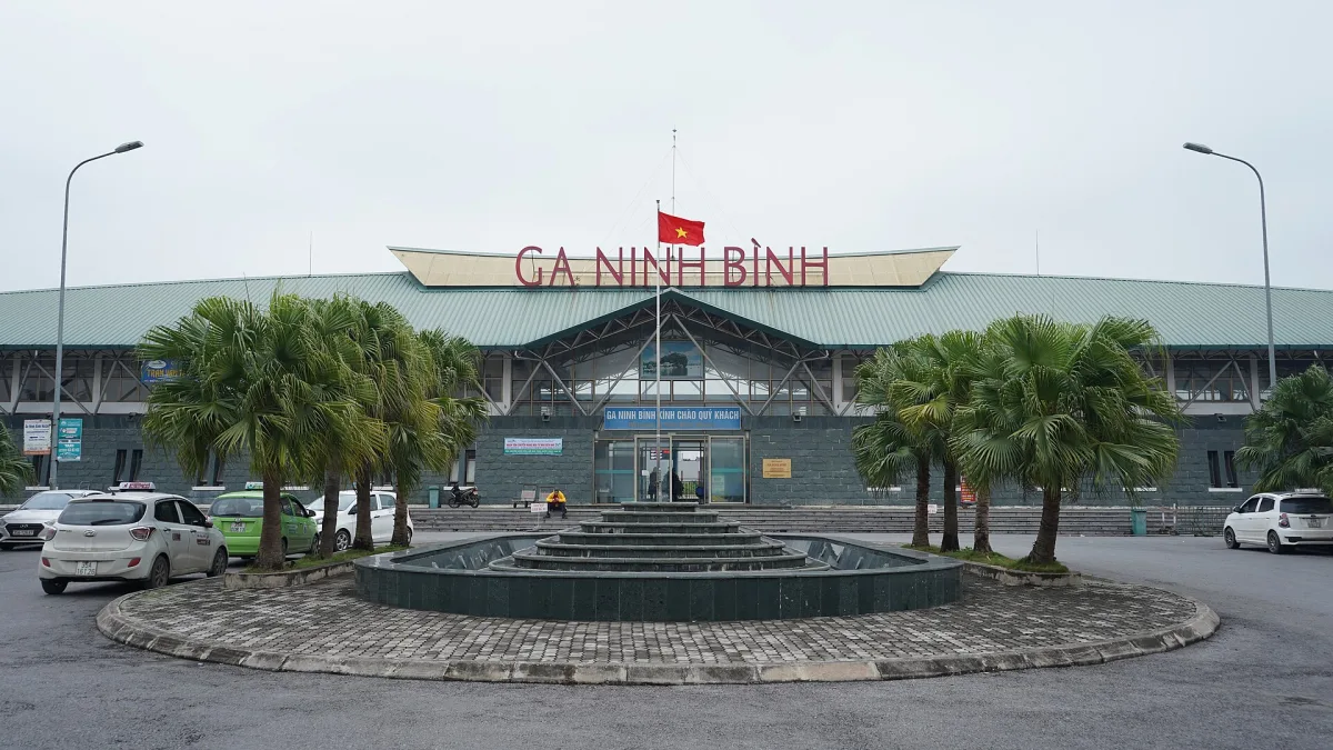 Façade de la gare de Ninh Bình : grand auvent, palmiers et taxis devant l'entrée