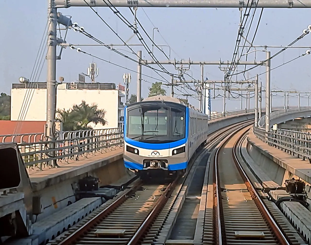 Rame bleue et grise de la ligne 1 du métro de Hô-Chi-Minh-Ville arrivant sur une voie aérienne, sous les caténaires