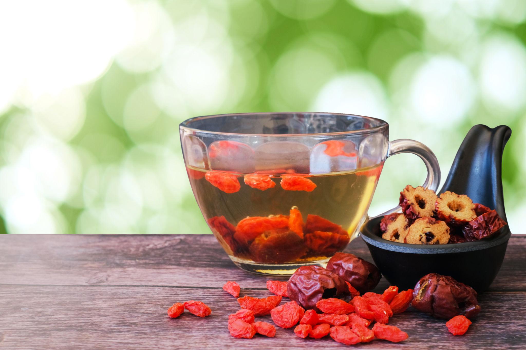 Tasse en verre avec gojis rouges et dattes séchées flottant dans un thé doré