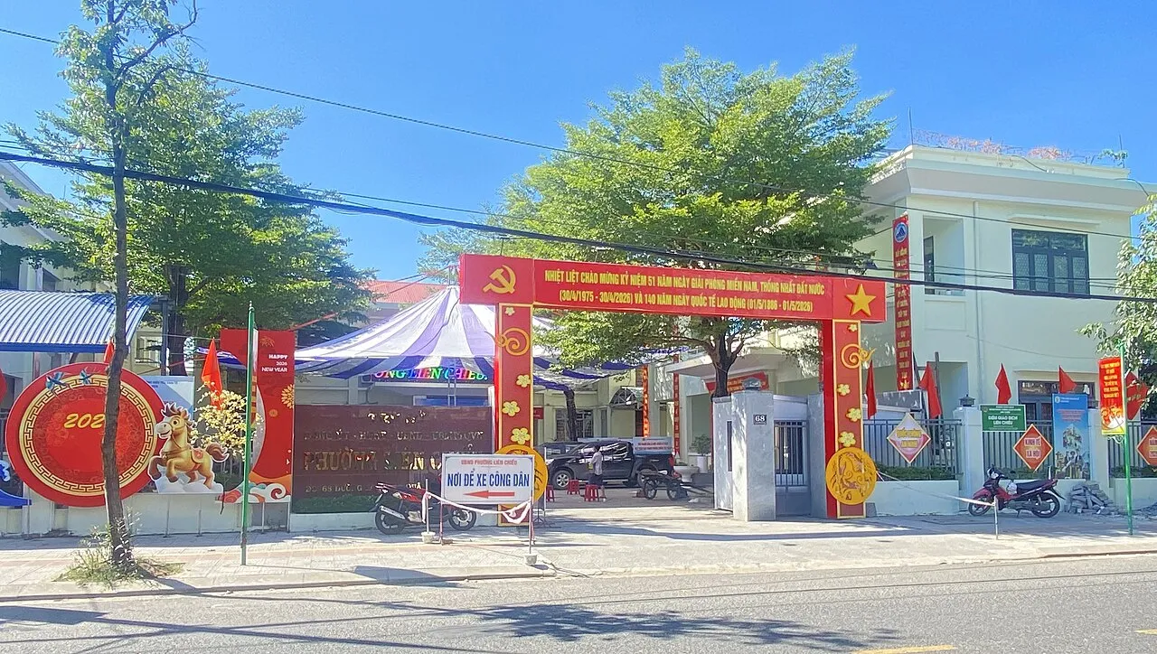 Entrée du siège du comité populaire (UBND) du quartier de Liên Chiểu à Đà Nẵng, avec un portique rouge, des drapeaux et un bâtiment blanc au fond