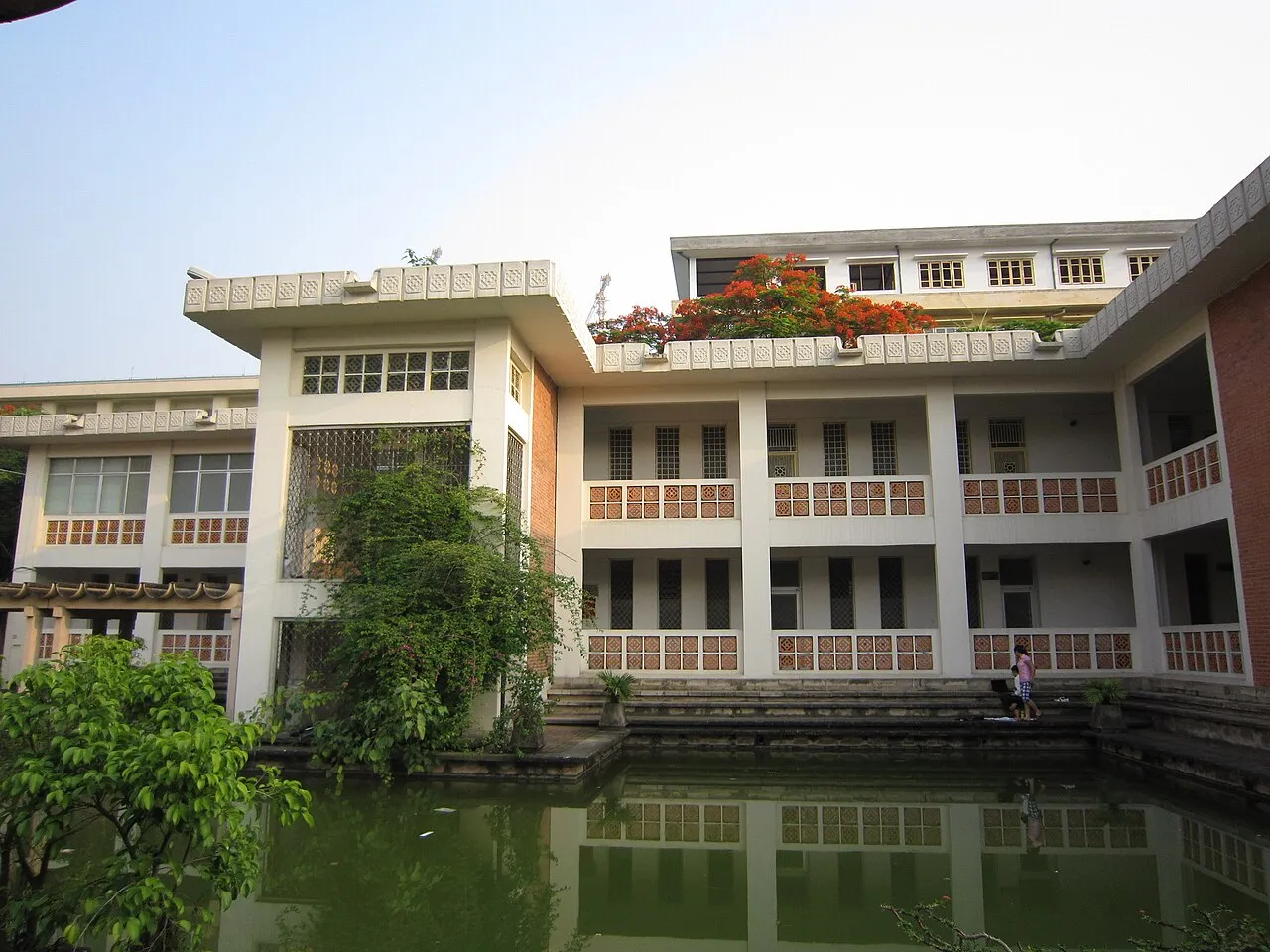 Bâtiment blanc à deux étages, avec coursives et balustrades ajourées, au bord d'un bassin, à l'Université de langues et d'études internationales de Hanoï